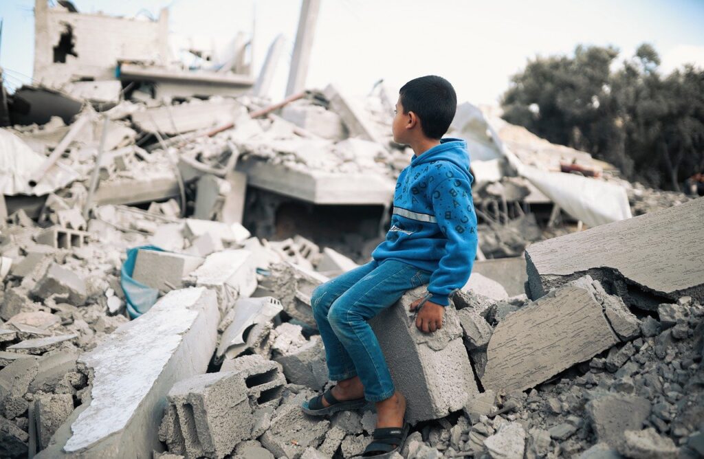 A young boy sits looking at rubble in Gaza